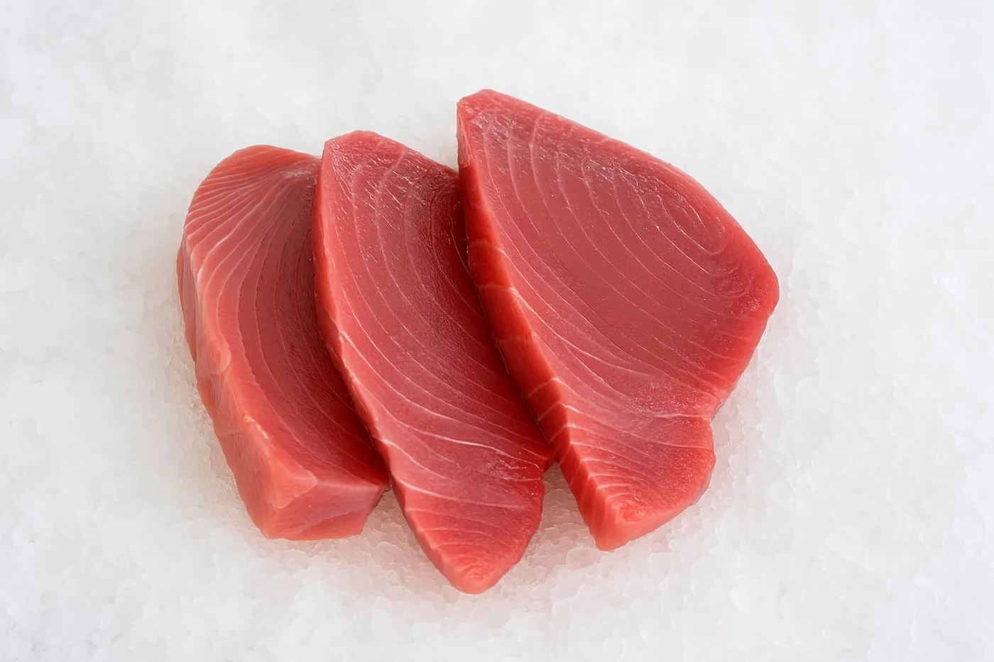 Three yellowfin tuna steaks fanned out on a white surface